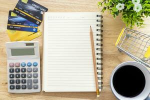 Credit card in Shopping cart with notebook,a pencil,flower pot tree,calculator on wooden background, Online banking Concept,Top view with copy space office table. photo