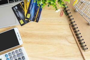 Credit card in Shopping cart with laptop,notebook,flower pot tree,smartphone and calculator on wooden background, Online banking Concept,Top view office table. photo