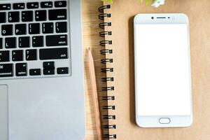 laptop with smartphone on notebook,a pencil and flower pot tree on wooden background,Top view office table. photo