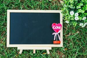 empty wooden blackboard and Flowerpot in square shape on green grass in the park background,Love concept with heart desktop. photo