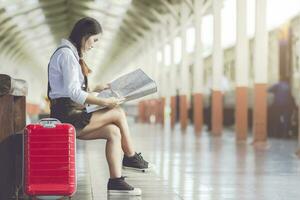 Asian woman pregnant sit on the bench look at the map with red suitcase at railway station travel,Holiday travel concept. photo