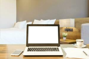 Laptop,smart phone and document on wooden table of defocused white pillow on bed decoration with light lamp in hotel bedroom interior background,Leisure and travel in the holiday concept. photo