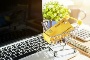 Credit card in Shopping cart with notebook,a pencil,flower pot tree,calculator on wooden background, Online banking Concept,Top view with copy space office table. photo