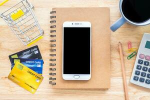 crédito Tarjetas,cuaderno,flor maceta Árbol,smartphone,compras carro y café taza en de madera fondo, en línea bancario concepto,arriba ver oficina mesa. foto