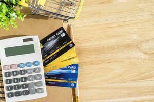 Credit card in Shopping cart with notebook,a pencil,flower pot tree,calculator on wooden background, Online banking Concept,Top view with copy space office table. photo