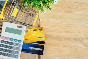 Credit card in Shopping cart with notebook,a pencil,flower pot tree,calculator on wooden background, Online banking Concept,Top view with copy space office table. photo