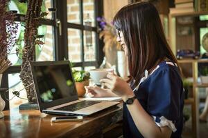 Mujer de negocios asiática sostiene una taza de café trabajando con un portátil en la cafetería como el fondo. foto