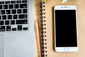 laptop with smartphone on notebook,a pencil and flower pot tree on wooden background,Top view office table. photo