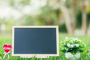 empty wooden blackboard and Flowerpot in square shape on green grass in the park background,Love concept with heart desktop. photo