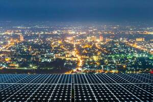 Solar panel or Photovoltaic modules solar power plant with cityscape over the light of city center background at night time, Alternative energy concept. photo