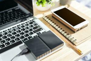 External Hard Disk on Laptop Keyboard with smartphone on notebook,a pencil and flower pot tree on wooden background,Top view office table. photo