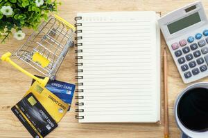 Credit card in Shopping cart with notebook,a pencil,flower pot tree,calculator on wooden background, Online banking Concept,Top view with copy space office table. photo