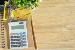 Credit card in Shopping cart with notebook,a pencil,flower pot tree,calculator on wooden background, Online banking Concept,Top view with copy space office table. photo