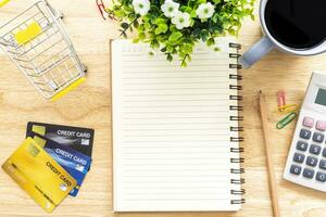 Credit card in Shopping cart with notebook,a pencil,flower pot tree,calculator on wooden background, Online banking Concept,Top view with copy space office table. photo