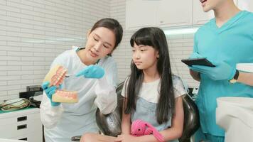 asiatisch weiblich pädiatrisch Zahnarzt und Assistent zeigen Zahnbürste zu wenig Mädchen mit Zähne Modell- im Dental Klinik, Wohlbefinden Hygiene, und Fachmann kieferorthopädisch Gesundheitswesen Arbeit im Kind Krankenhaus. video