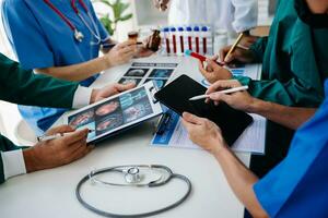 Medical team having a meeting with doctors in white lab coats and surgical scrubs seated at a table discussing a patients working online using computers in the medical industry photo