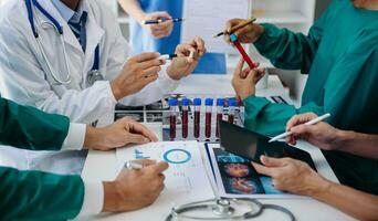 Medical team having a meeting with doctors in white lab coats and surgical scrubs seated at a table discussing a patients working online using computers in the medical industry photo