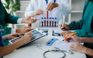 Medical team having a meeting with doctors in white lab coats and surgical scrubs seated at a table discussing a patients working online using computers in the medical industry photo