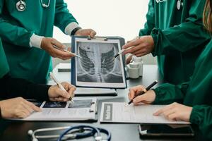 médico equipo teniendo un reunión con doctores en blanco laboratorio abrigos y quirúrgico matorrales sentado a un mesa que se discute un pacientes trabajando en línea utilizando ordenadores en el médico foto