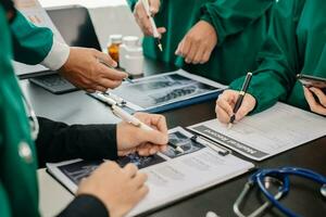 Medical team having a meeting with doctors in white lab coats and surgical scrubs seated at a table discussing a patients working online using computers in the medical photo