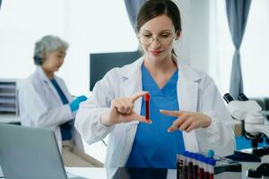 Confident young Caucasian female doctor in white medical uniform sit at desk working on computer. Smiling use laptop write in medical journal in clinic. photo