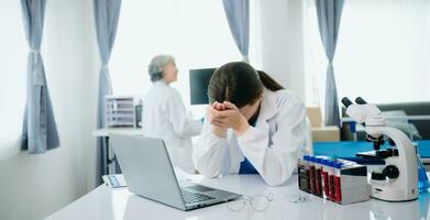 Confident young Caucasian female doctor in white medical uniform sit at desk working on computer. Smiling use laptop write in medical journal photo