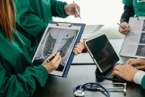 médico equipo teniendo un reunión con doctores en blanco laboratorio abrigos y quirúrgico matorrales sentado a un mesa que se discute un pacientes trabajando en línea utilizando ordenadores en el médico foto