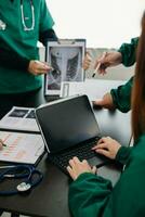 médico equipo teniendo un reunión con doctores en blanco laboratorio abrigos y quirúrgico matorrales sentado a un mesa que se discute un pacientes trabajando en línea utilizando ordenadores en el médico foto