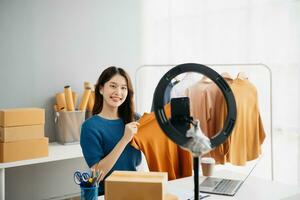 Asian lady blogger showing clothes in front of the camera to recording vlog video live streaming at her shop. photo