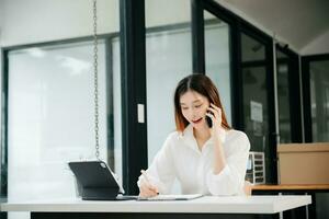 Young beautiful woman typing on tablet and laptop while sitting at the working white table modern office photo