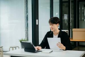 confidente asiático hombre con un sonrisa en pie participación bloc y tableta a el oficina. foto