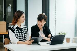 Two Asian businesswoman and man discuss investment project working and planning strategy with tablet laptop computer in office. photo