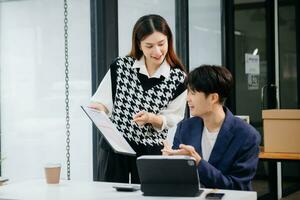 Two Asian businesswoman and man discuss investment project working and planning strategy with tablet laptop computer in office. photo