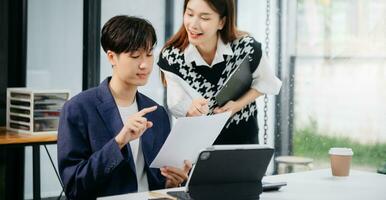 Two Asian businesswoman and man discuss investment project working and planning strategy with tablet laptop computer in office. photo