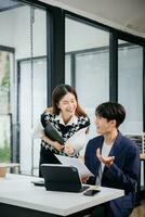 Two Asian businesswoman and man discuss investment project working and planning strategy with tablet laptop computer in office. photo