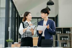 Two Asian businesswoman and man discuss investment project working and planning strategy with tablet laptop computer in office. photo