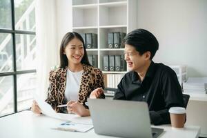 Asian business colleague business presents and explains and using laptop and tablet. Teamwork, financial marketing team,   while sitting in modern office room. photo