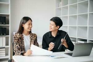 Asian business colleague business presents and explains and using laptop and tablet. Teamwork, financial marketing team,   while sitting in modern office room. photo