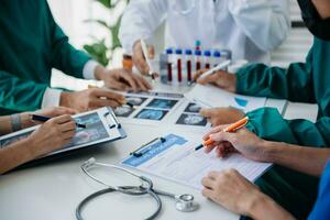 Medical team having a meeting with doctors in white lab coats and surgical scrubs seated at a table discussing a patients working online using computers in the medical industry photo