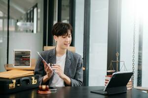 Asian female lawyer chatting online with client on laptop, smartphone  discussing details of lawsuit. in modern office photo