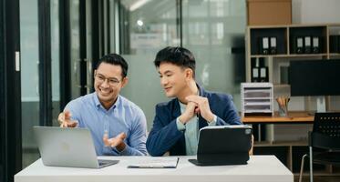 Two Asian businessman discuss investment project working and planning strategy with tablet laptop computer in modern office. photo