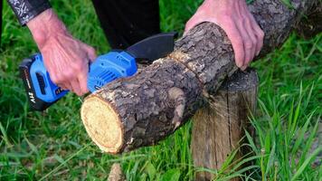 Hand-held portable camping electric saw on a battery for cutting firewood and wood. Close-up, a hand sawing a log, splinters flying video