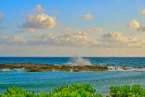 un parcialmente nublado primavera Mañana en el bahamas como olas choque en contra el rock pared foto