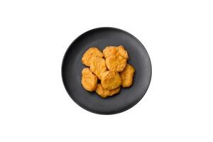 Delicious crispy chicken nuggets with salt and spices on a dark concrete background photo