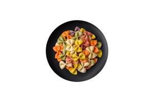 Raw farfalle pasta in different colors on a dark concrete background photo