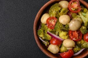 Delicious fresh salad with broccoli, cherry tomatoes, mushrooms, onions, salt, spices and herbs photo