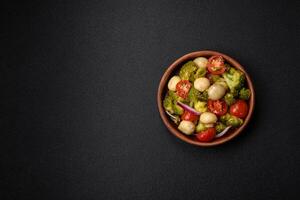 Delicious fresh salad with broccoli, cherry tomatoes, mushrooms, onions, salt, spices and herbs photo