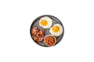 A delicious nutritious healthy breakfast with fried eggs, bacon, beans, a glass of juice, oat cookies, milk and jam photo