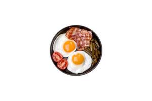 Tasty breakfast consists of eggs, bacon, beans, tomatoes, with spices and herbs photo