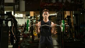 A portrait of a male weightlifter in black sportswear. He does barbell fitness workout in the modern gym. photo